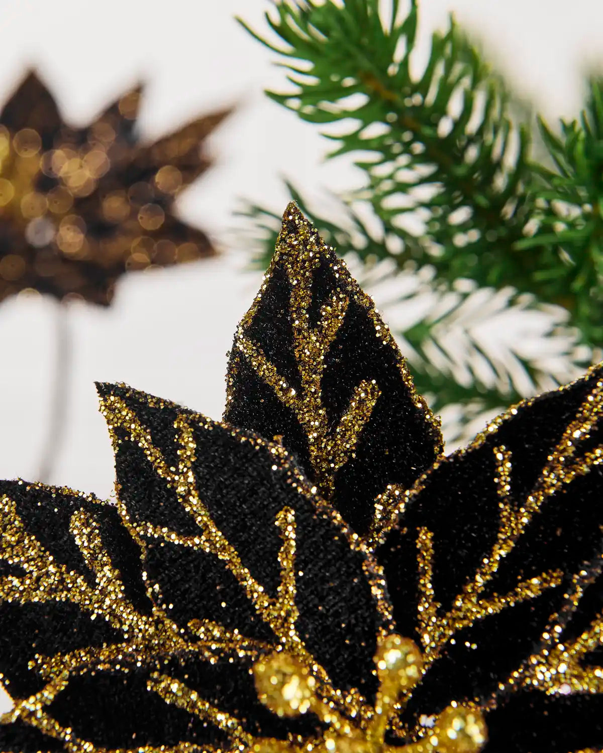 Close-up view of the layered black poinsettia petals covered in gold glitter detailing and a sparkling gold center.