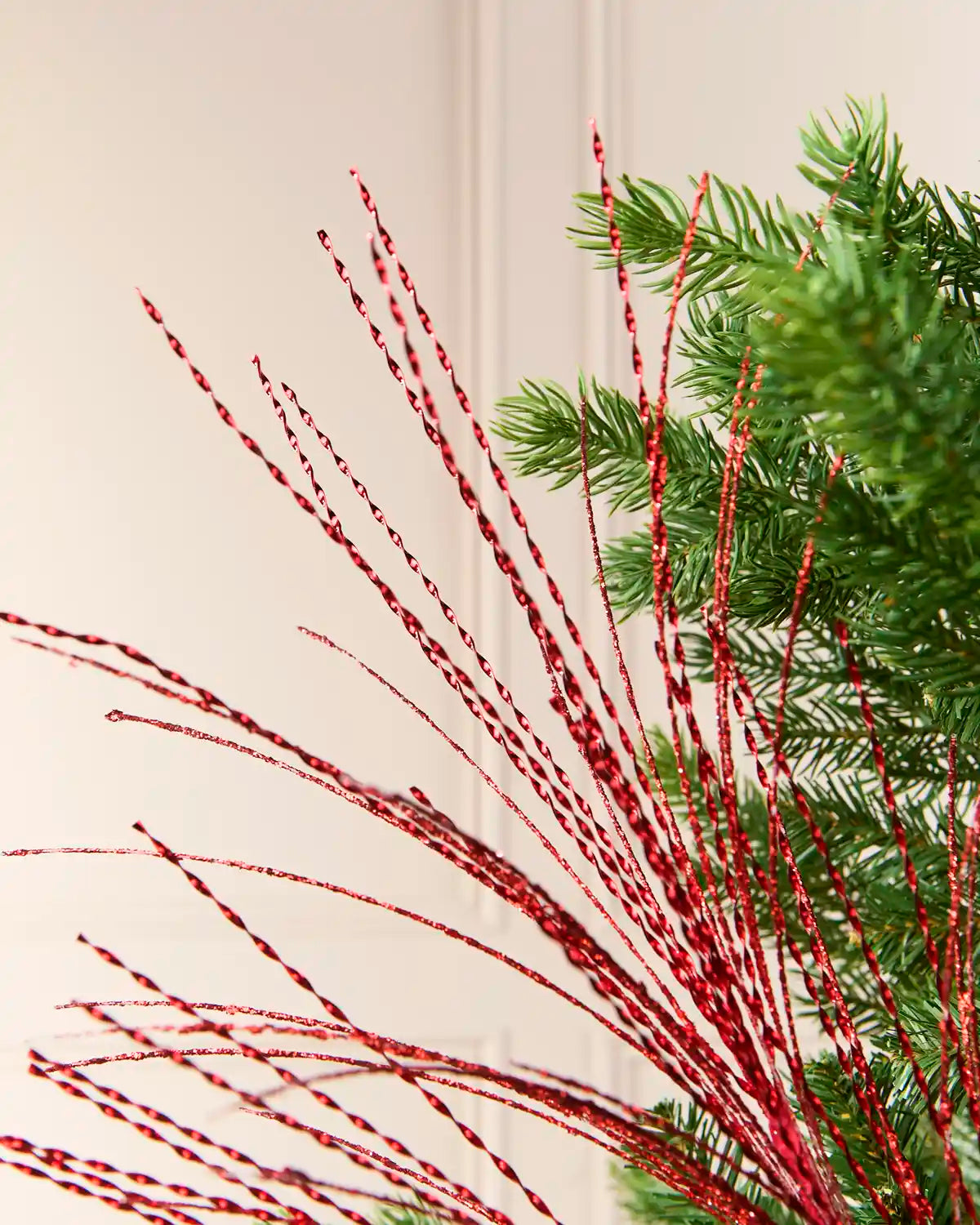 Close-up view of the red glitter strands of a Christmas tree fountain spray, arranged among green Christmas tree branches.
