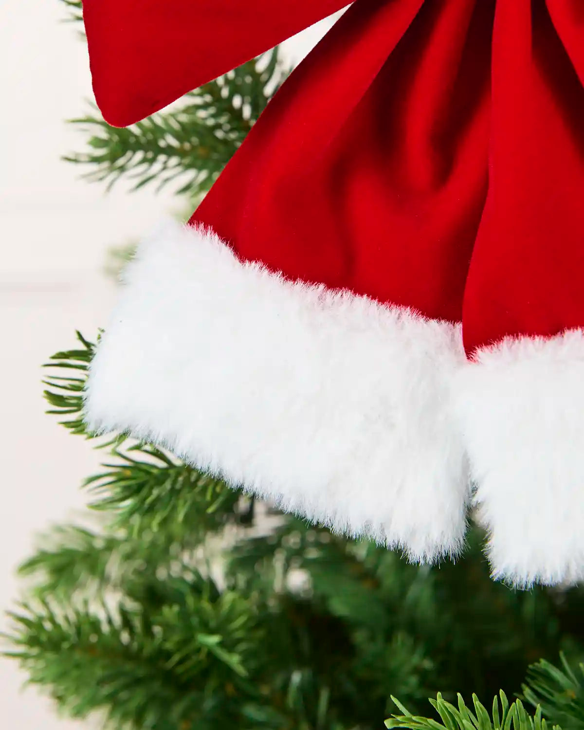 Close-up white cuff on velvet Santa bow hanging from Christmas tree branch