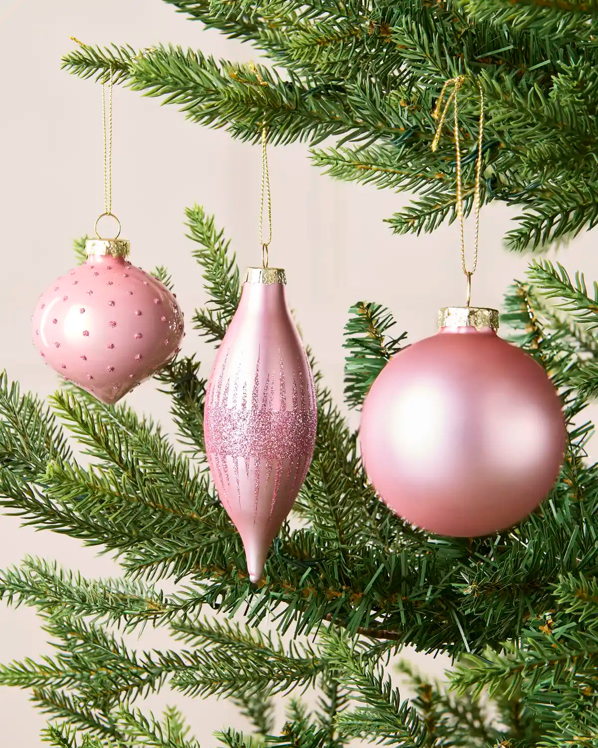 Close Up of Pink glass baubles hanging from Christmas tree branches in teardrop, onion and classic round shapes with glitter detailing.