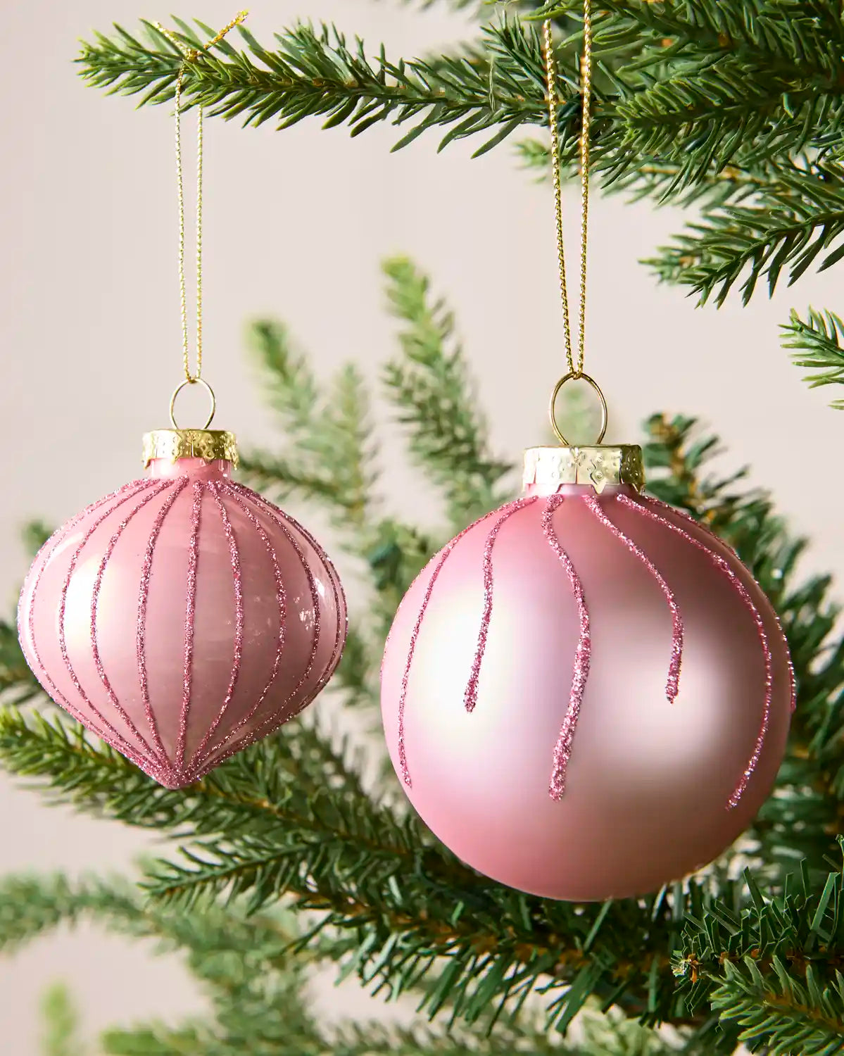 Close Up of Pink glass onion and round bauble hanging from Christmas tree branch with glitter detailing