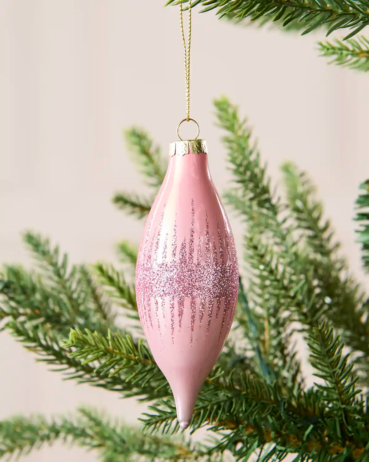 Close Up of Pink glass teardrop bauble hanging from Christmas tree branch with glitter detailing