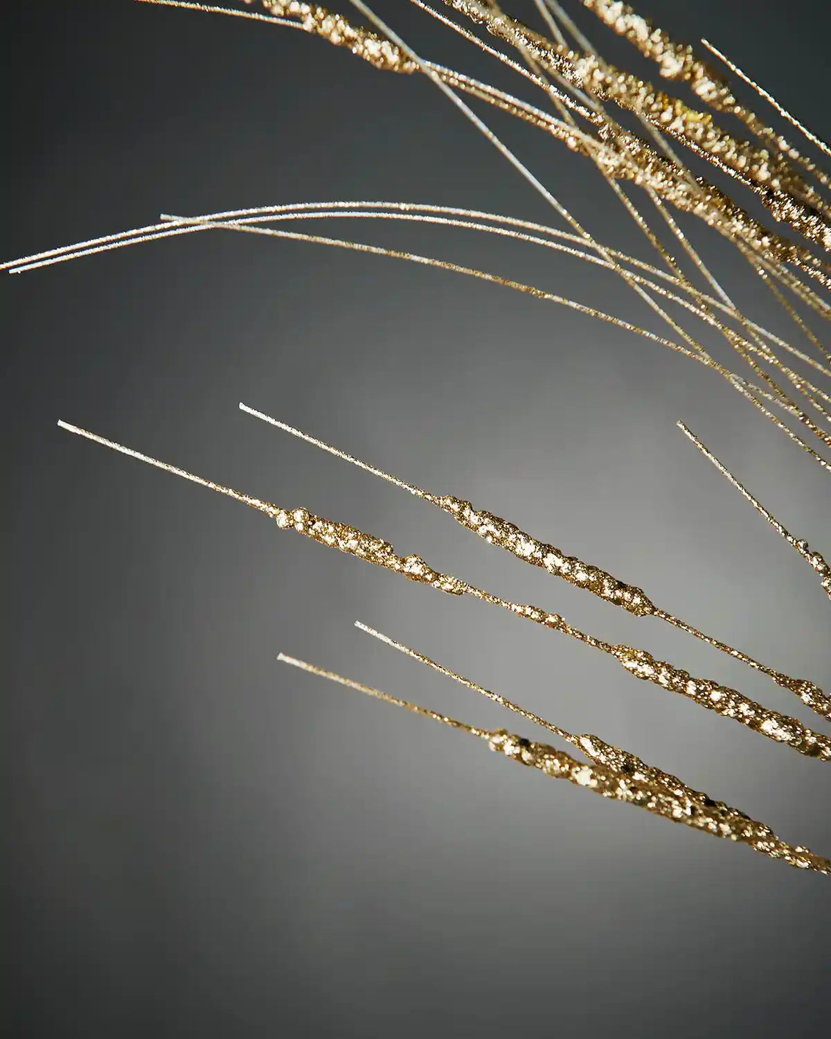 Close-up of 100cm gold glitter wispy spray in front of grey background highlighting sparkle