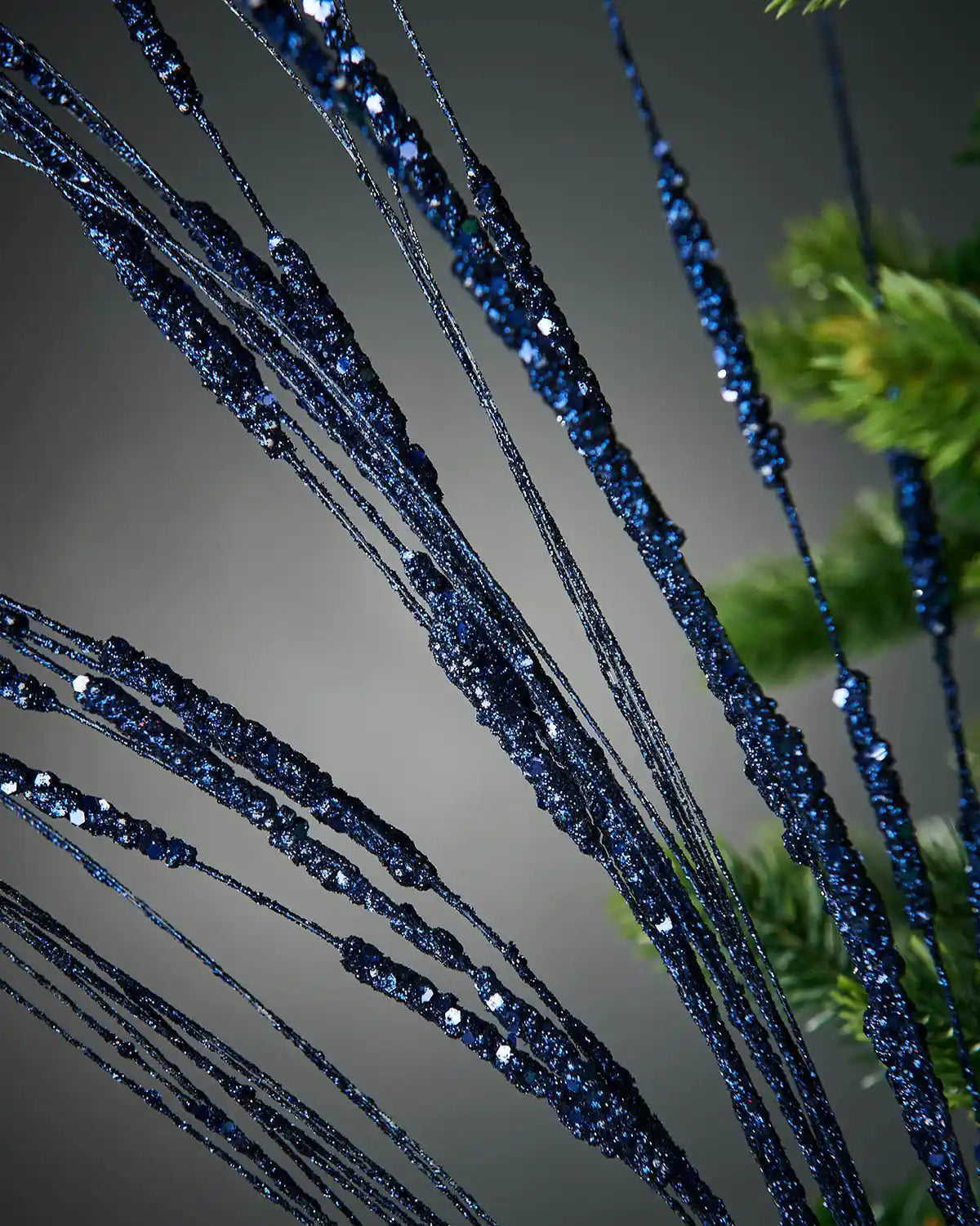 Close-up image of 100cm navy blue glitter wispy tree spray on Christmas tree in front of grey background