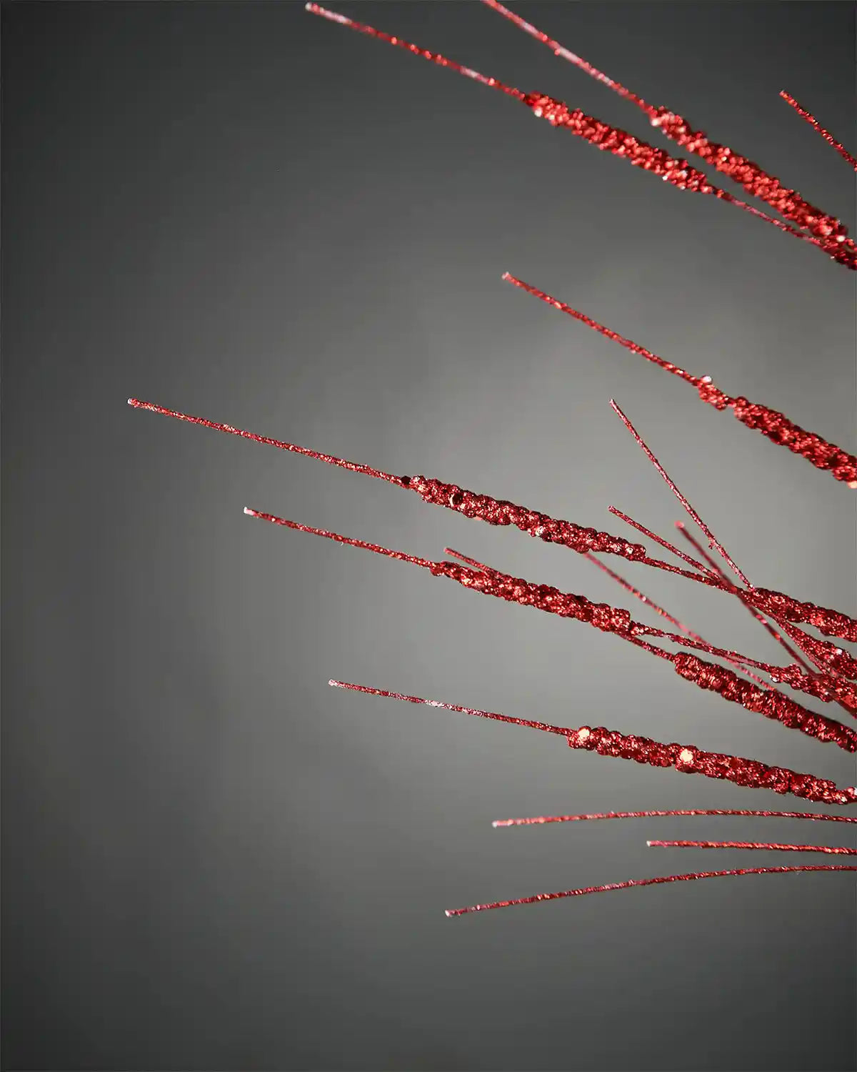 Close-up of 100cm red glitter wispy spray in front of grey background highlighting sparkle