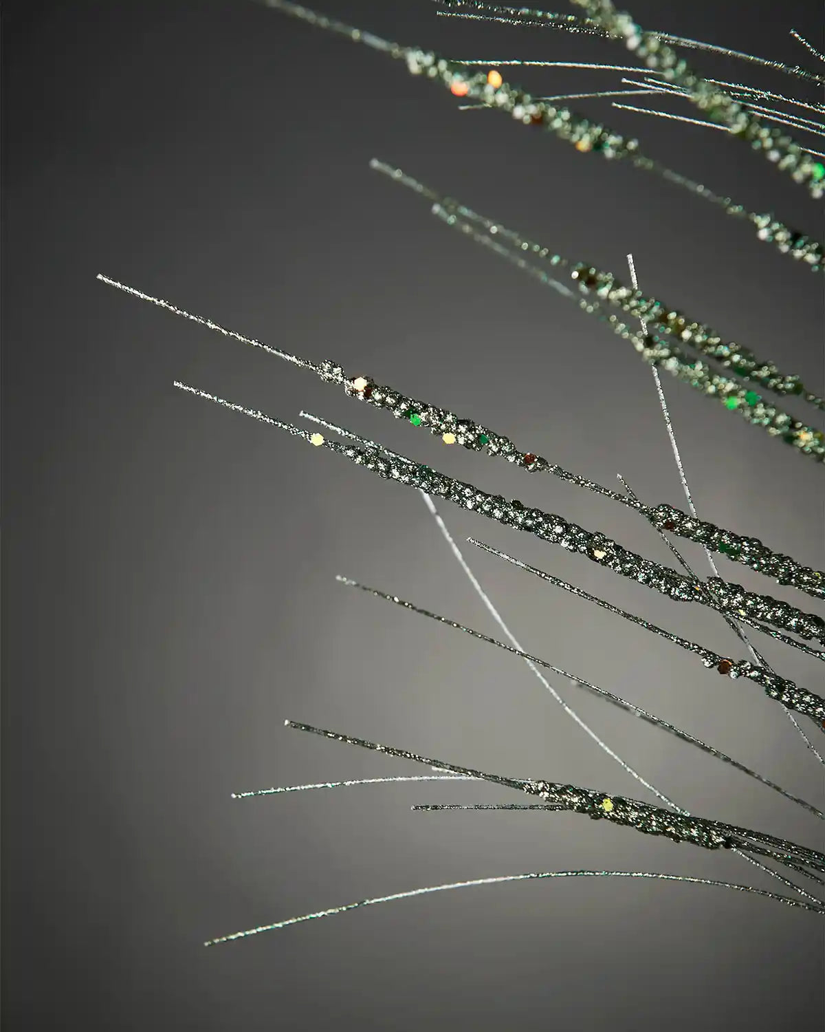 Close-up of 100cm sage green glitter wispy spray in front of grey wall background highlighting sequin detail