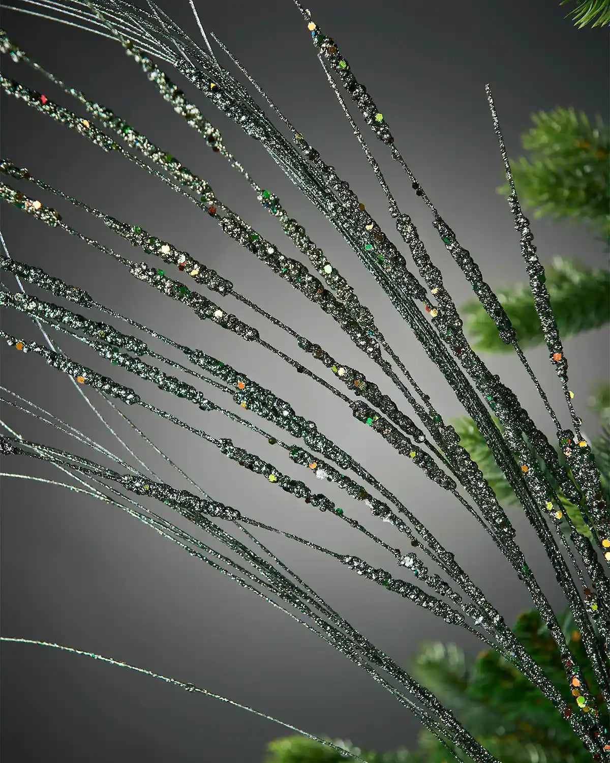 Close-up view of 100cm sage green glitter wispy spray in front of grey wall background highlighting sequin detail