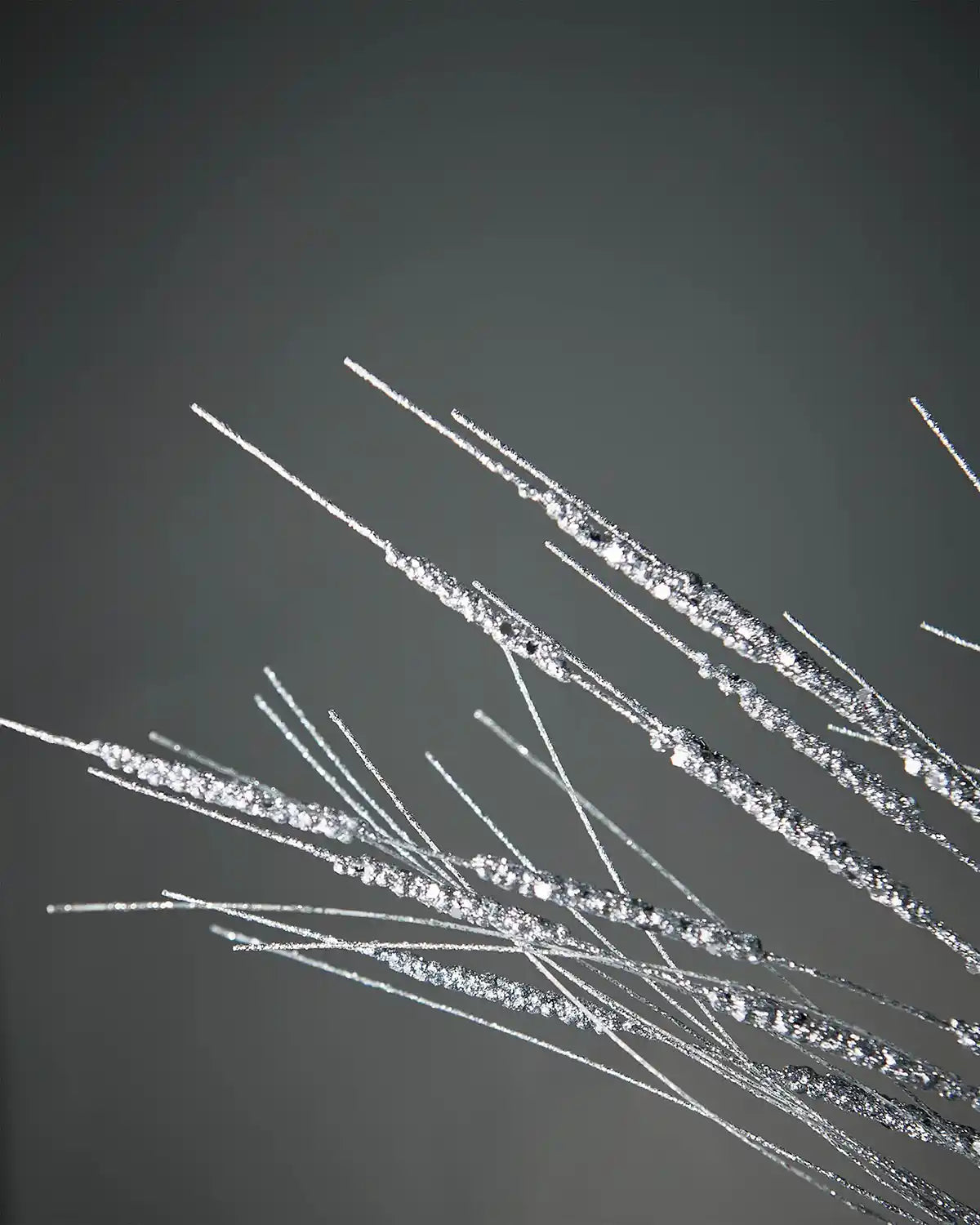 Close-up image of 100cm silver glitter wispy spray in front of grey background highlighting sparkle
