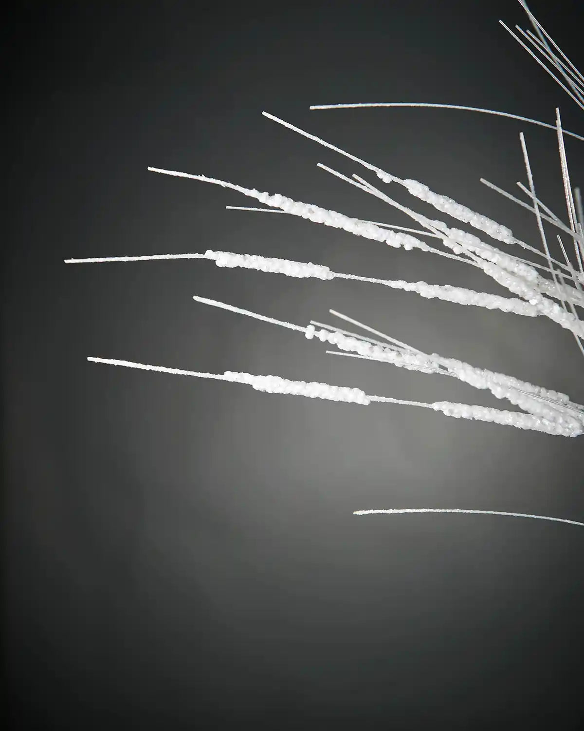 Close-up of 100cm white glitter wispy tree spray in front of grey background highlighting sequin accents