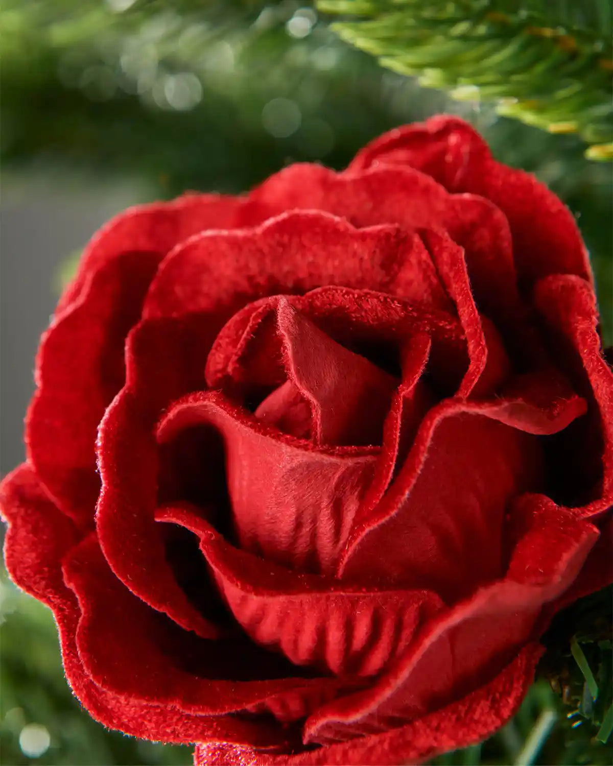 Close-up of a 10cm red artificial rose flower attached to a Christmas tree highlighting velvet style petals