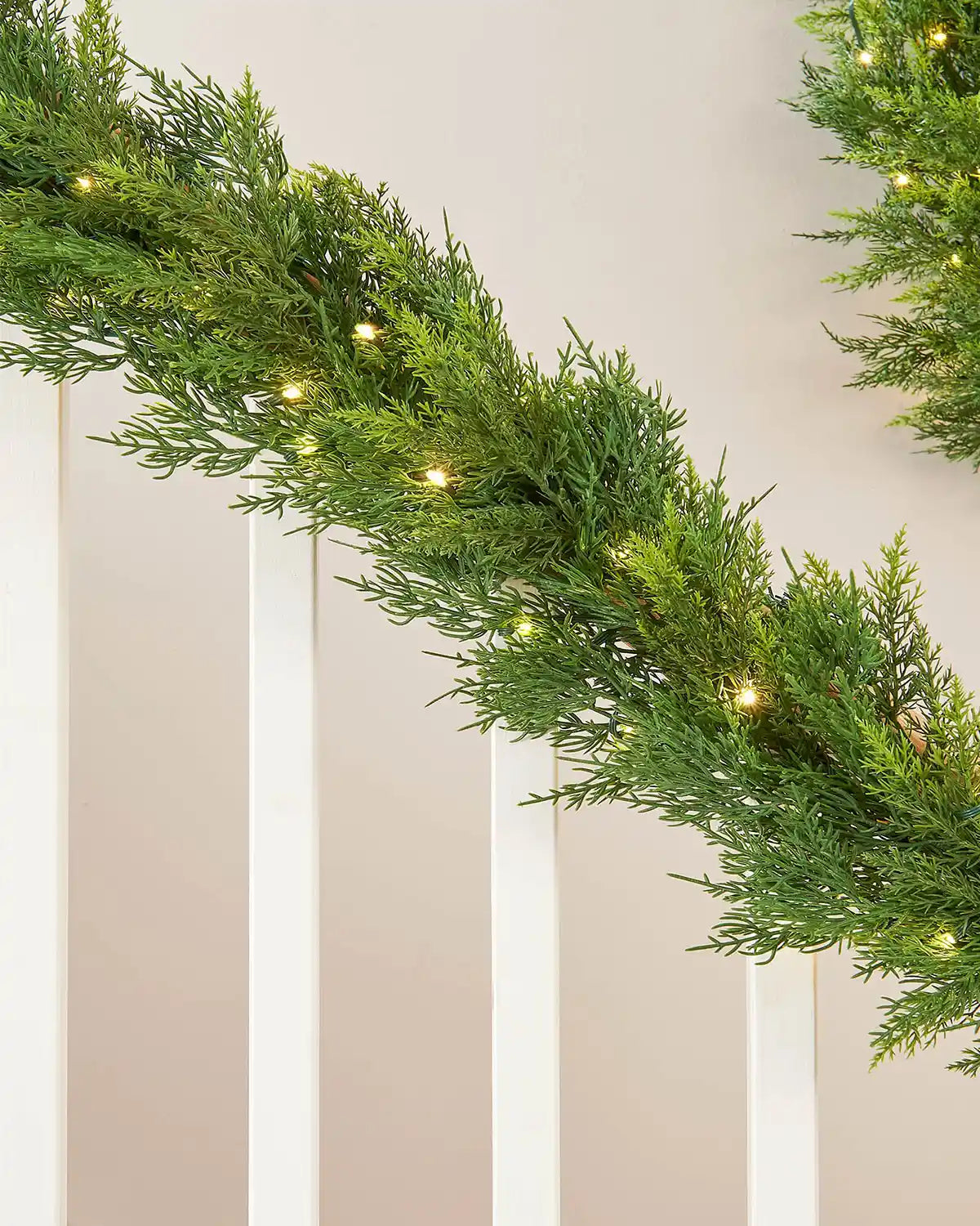 Close-up of 12ft pre-lit cypress fir garland with warm white light setting on white wooden staircase with preview of matching wreath