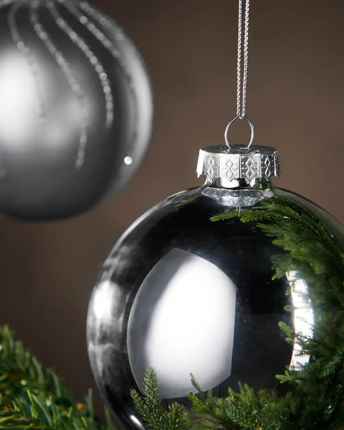 Close up 2 Silver Christmas ornament hanging on a tree branch with a brown background