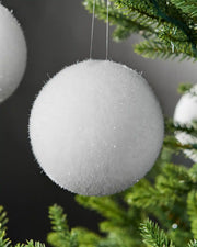 Close up 2 snowball baubles hanging on a Christmas tree branch against a Grey background