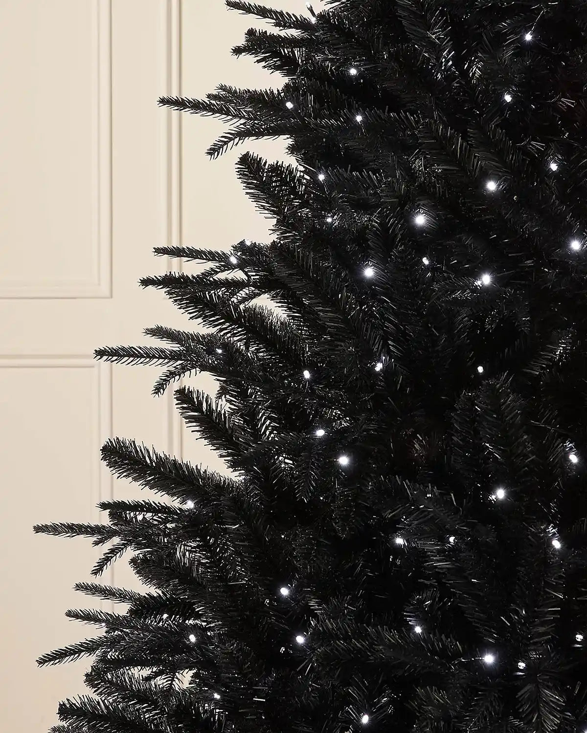Close-up of 7ft pre-lit black pine Christmas tree with bright white light setting in front of white panelling background
