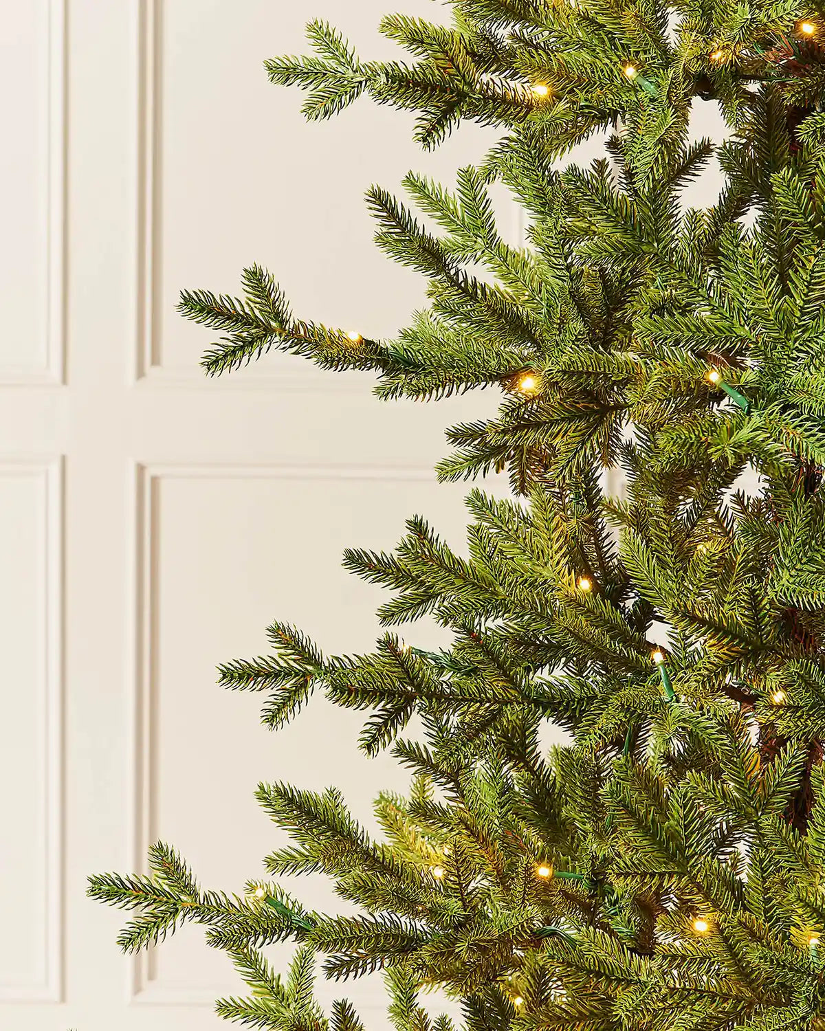 Close-up of 7ft pre-lit nordic pine Christmas tree with warm white light setting in front of white panelling