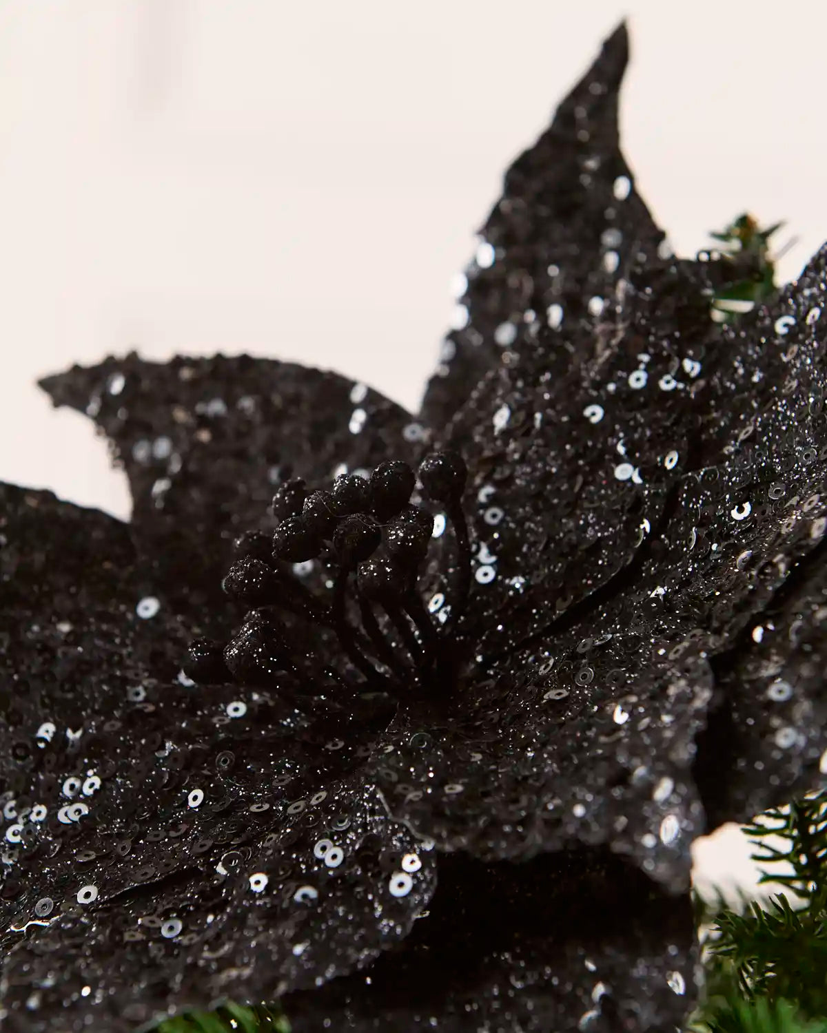 Close up Black Sequin Artificial Poinsettia showing sequin detailing and a blurry cream background
