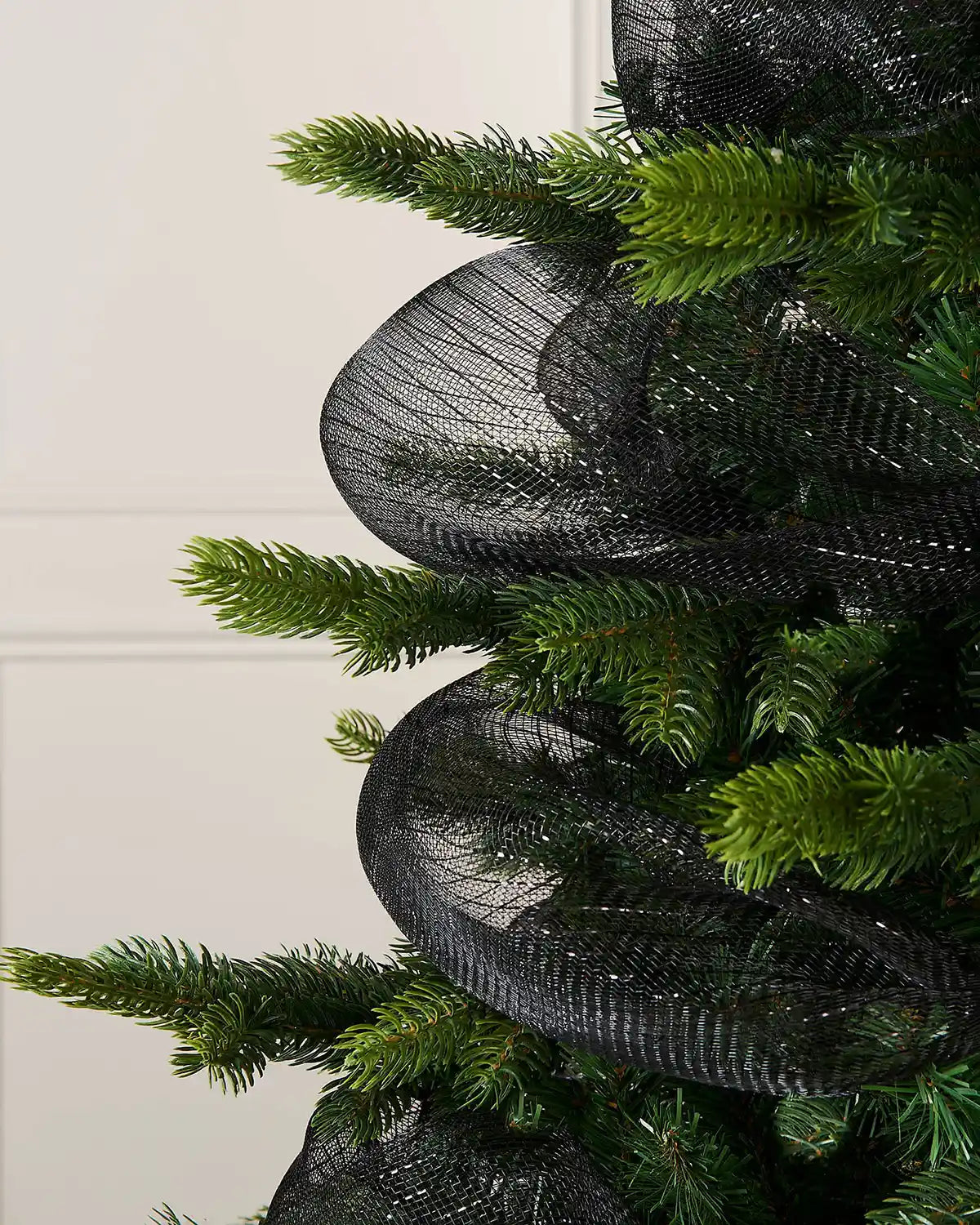 Close up Black mesh ribbon wrapped around Christmas tree against a cream background
