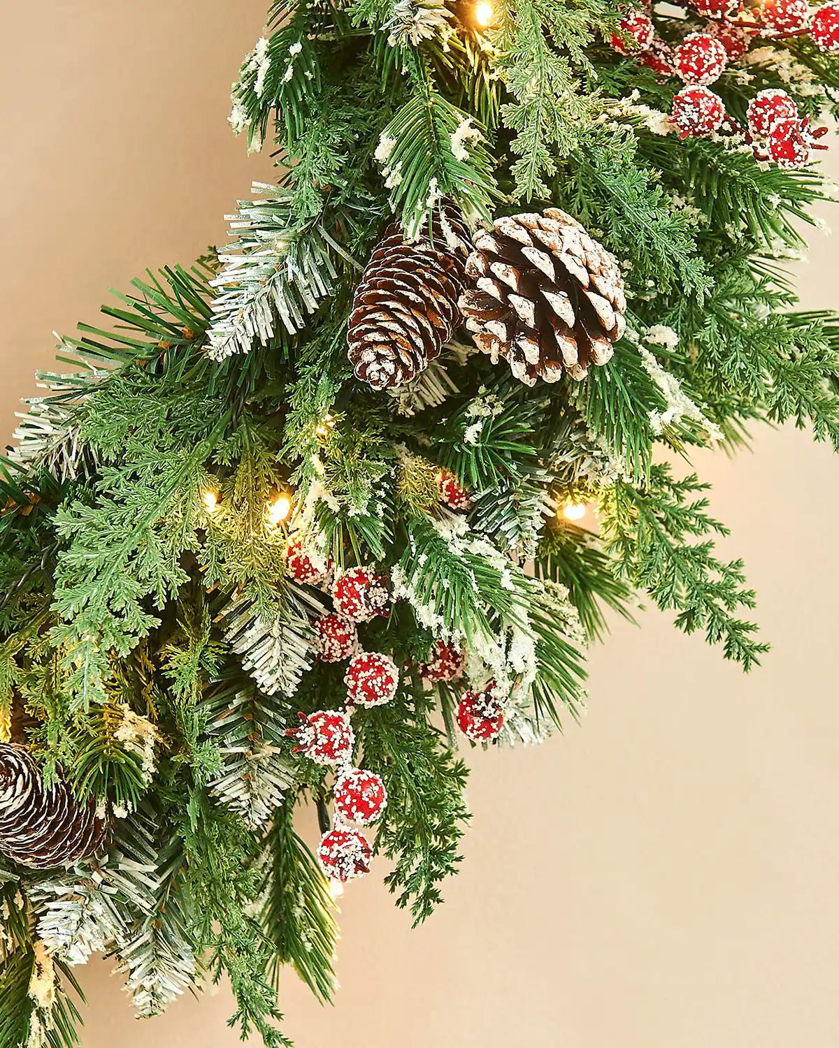 Close up Decorative Christmas wreath with greenery, pinecones, and red berries on a beige background