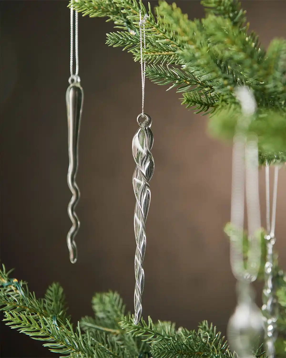 Close up Decorative glass icicle ornaments hanging from a Christmas tree branch against a brown background