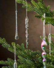 Close up Iridescent icicle ornaments hanging on a Christmas tree branch against a brown background