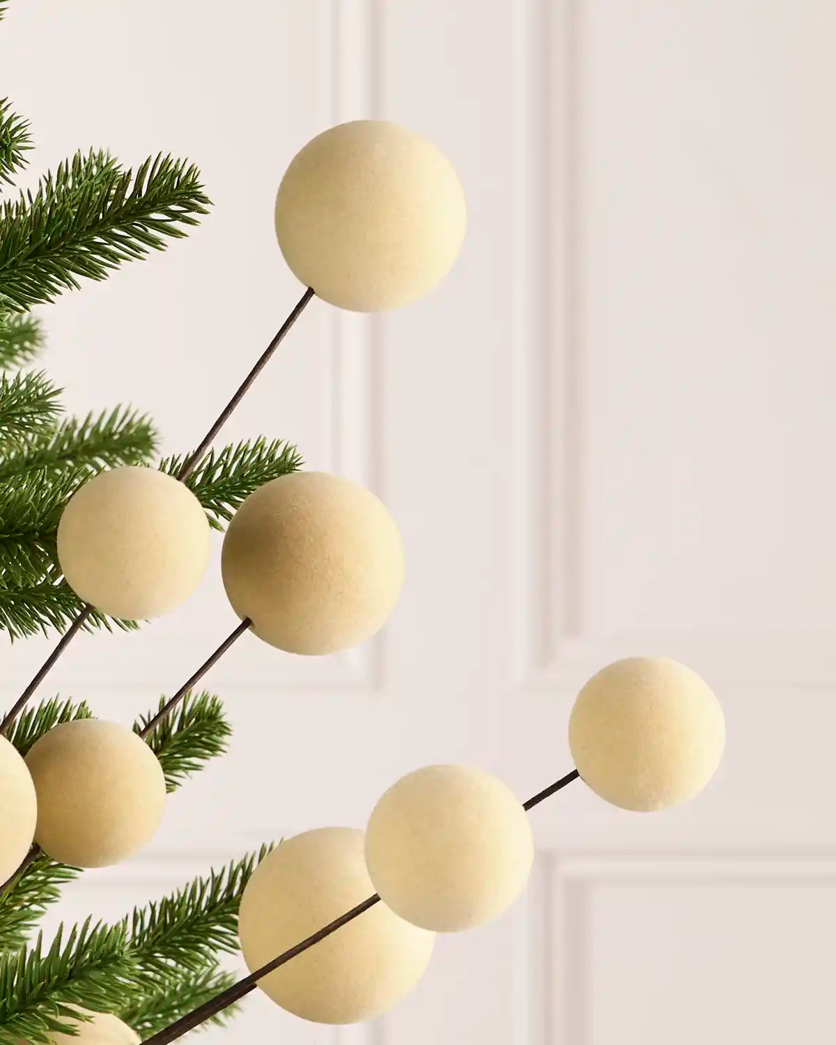 Close up Latte coloured velvet bauble pick on dark brown stems hanging from a Christmas tree against a light background
