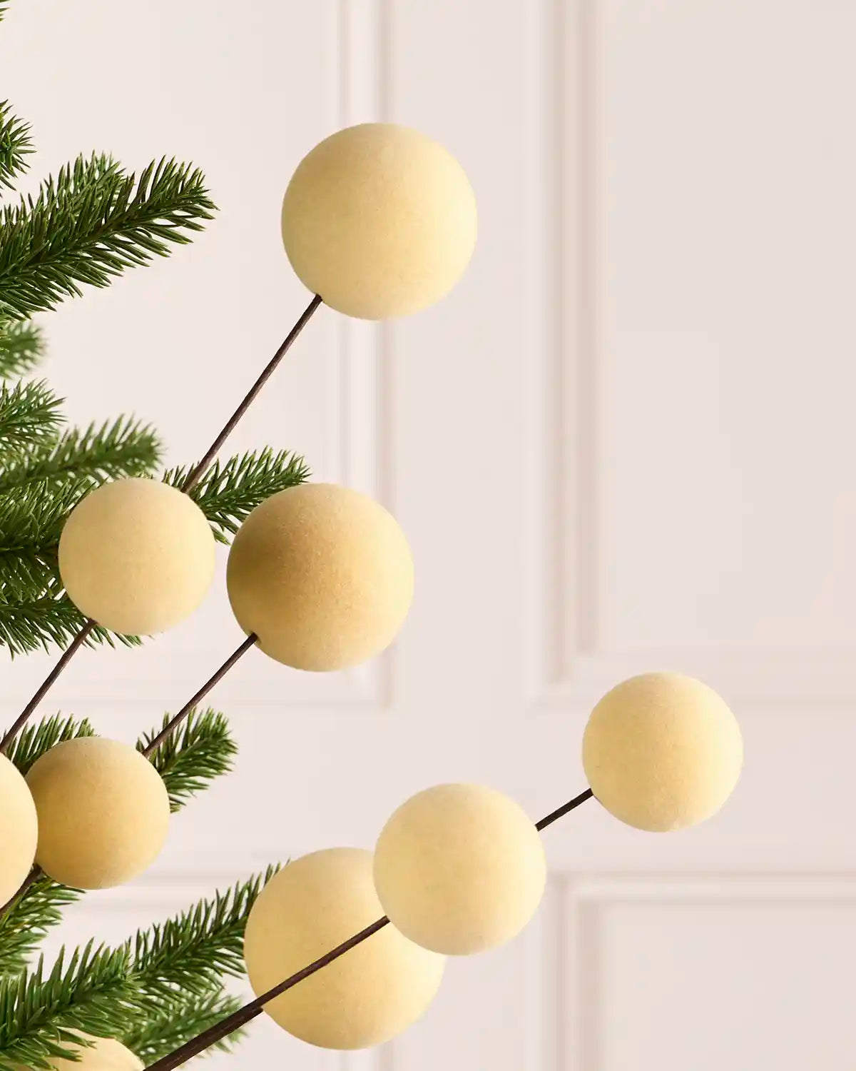 Close up Latte coloured velvet bauble pick on dark brown stems hanging from a Christmas tree against a light background
