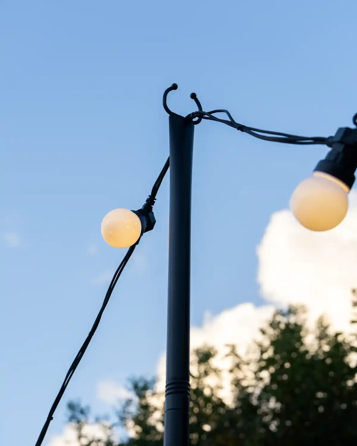 Close up Outdoor light pole holding up festoon lights with cloudy blue sky in the background