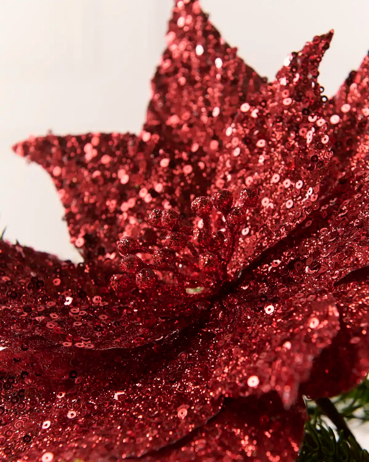 Close up Red Sequin Artificial Poinsettia showing sequin detailing and a blurry cream background