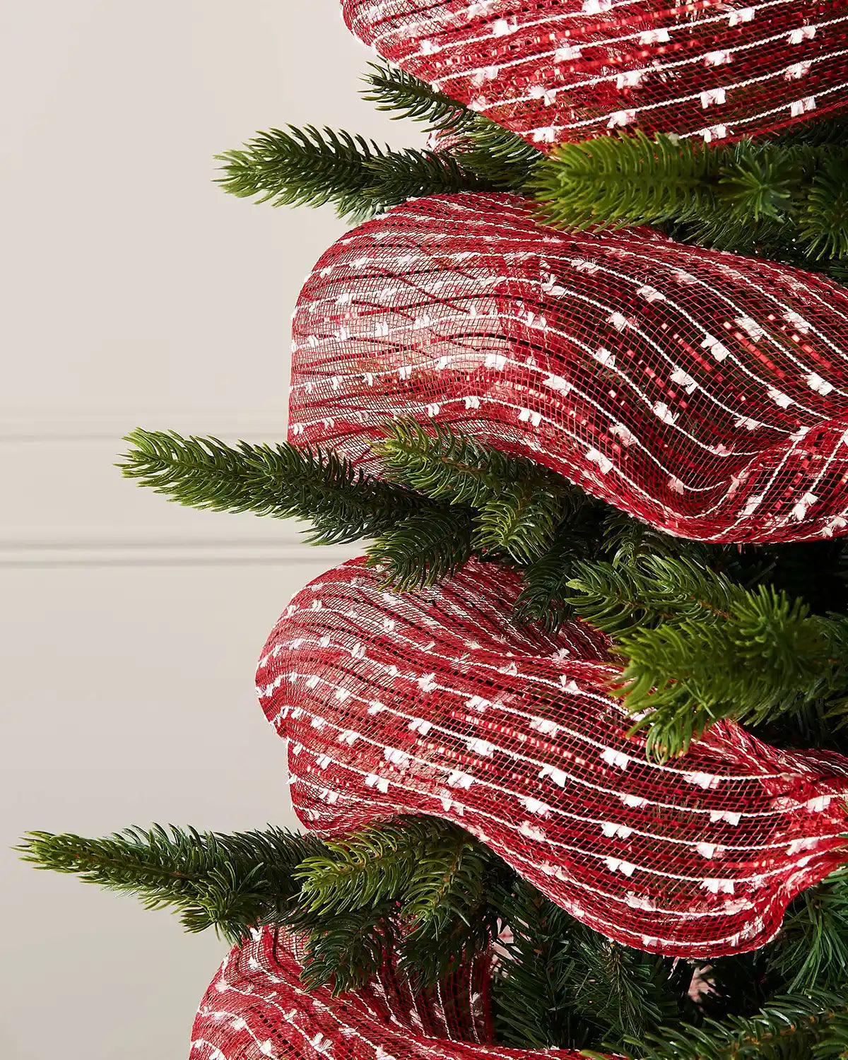 Close up Red and white mesh decorative roll wrapped around a Christmas tree against a cream panel wall