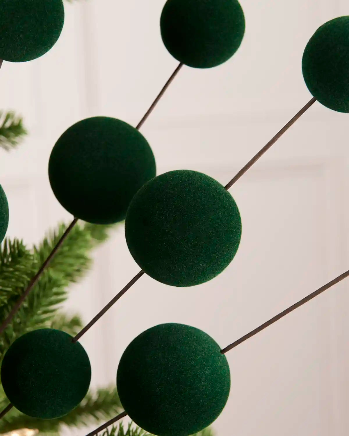 Close up Sage green velvet bauble pick with seven velvet baubles against a light background and a blurred Christmas tree branch