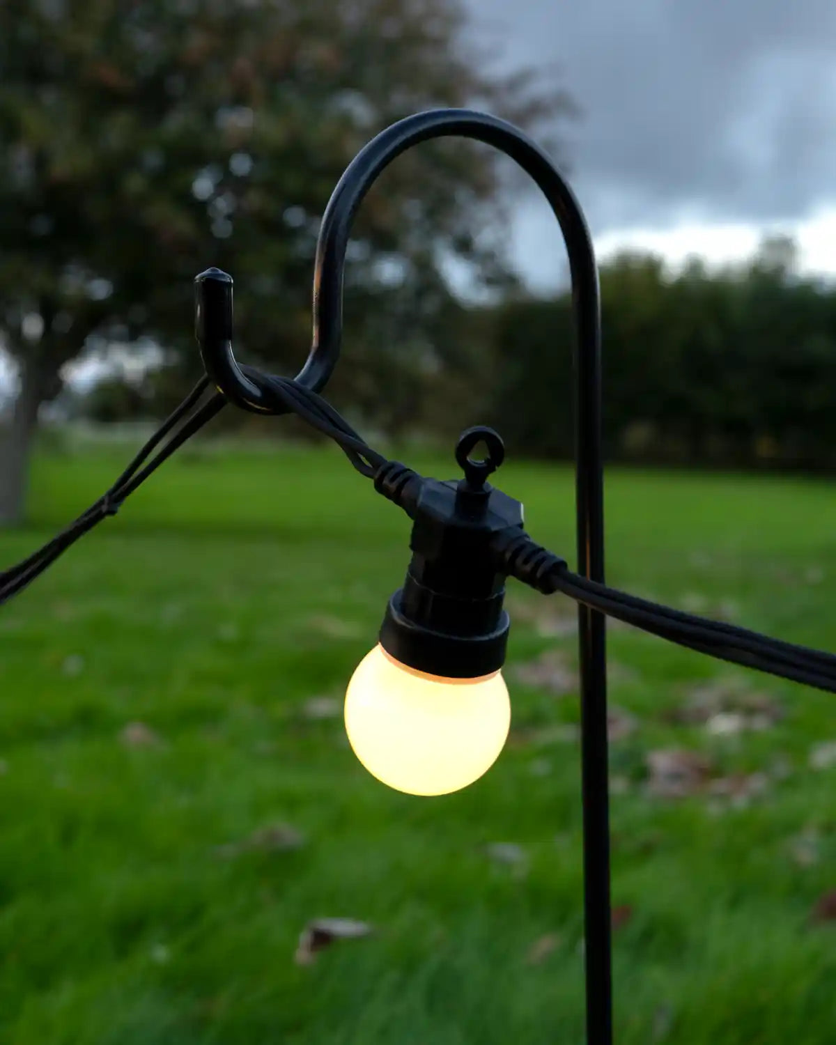 Close up Shepherd’s hook garden stake with a curved black metal top supporting outdoor string light