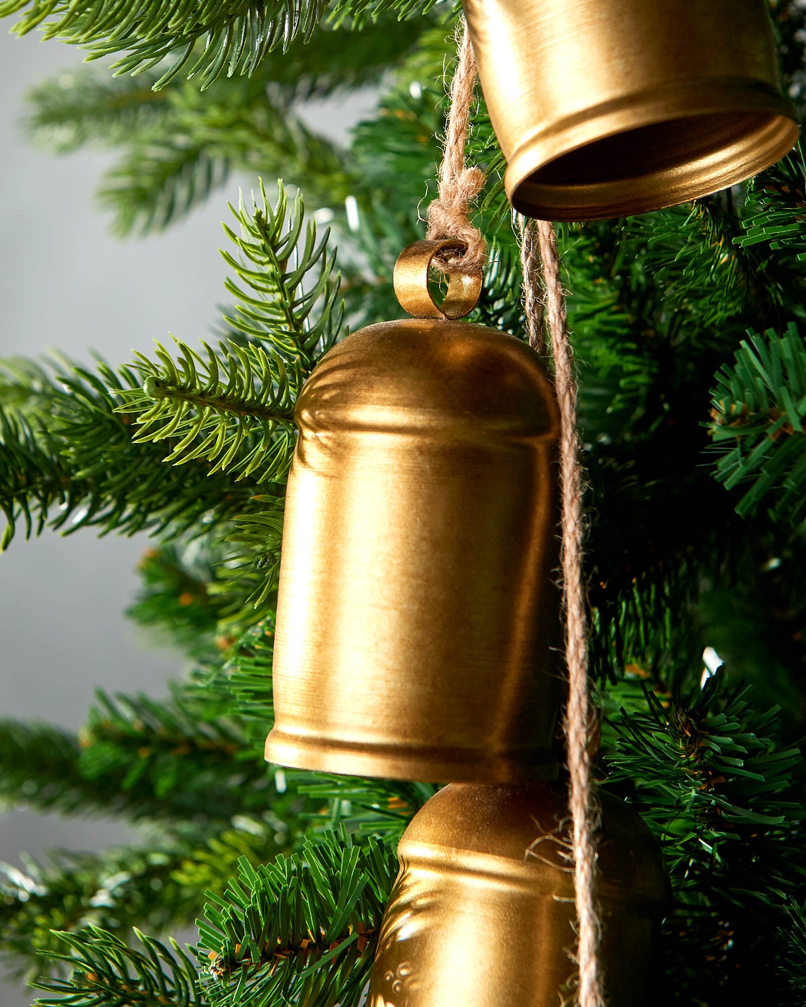 Close-up of antique-style gold hanging bells on Christmas tree in front of grey wall
