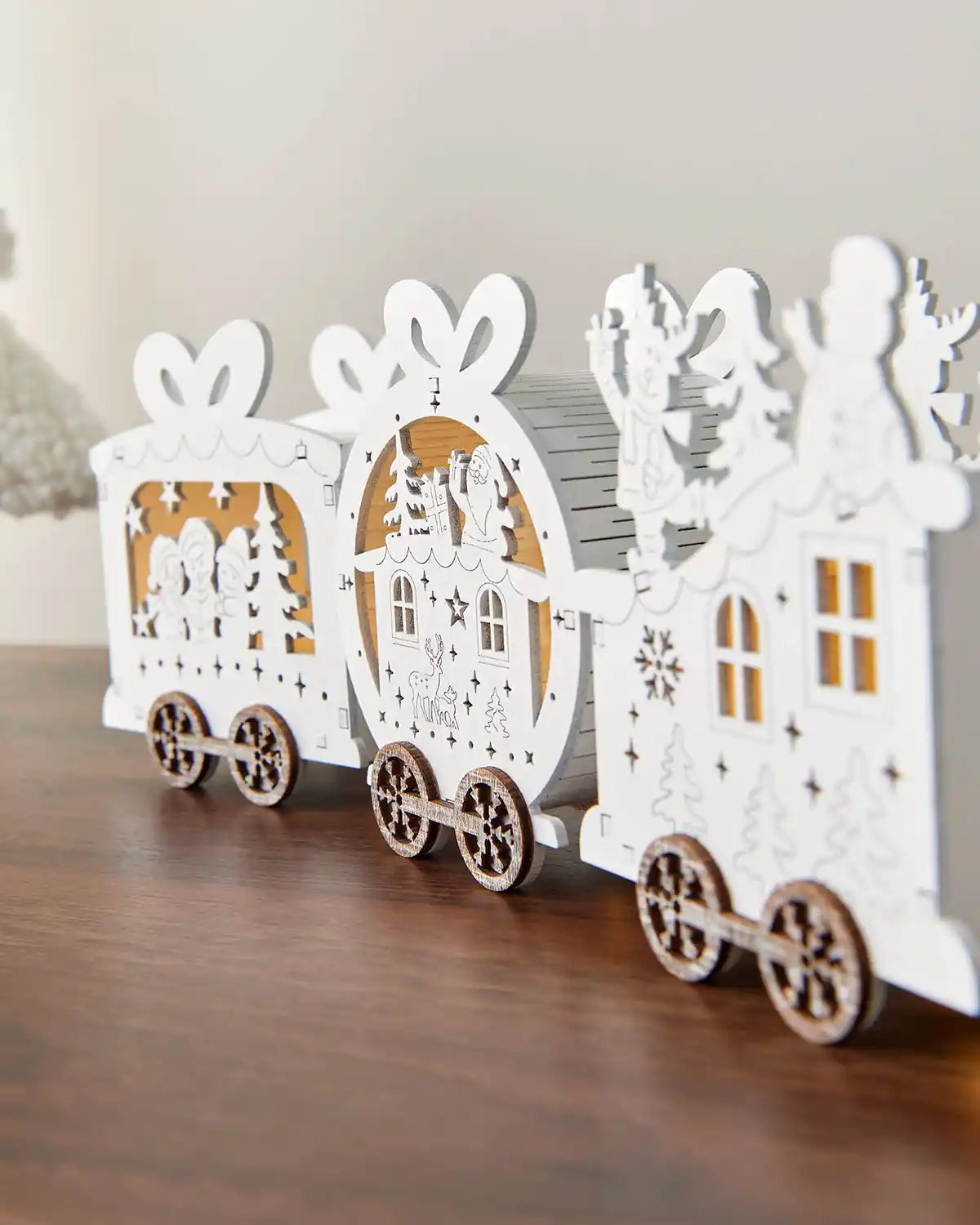 Close-up of back of pre-lit white wooden train decoration on dark wood surface in front of white wall