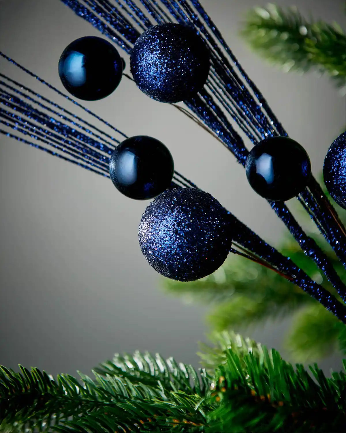 Close-up of baubles on navy blue glitter bauble spray on tree in front of grey background