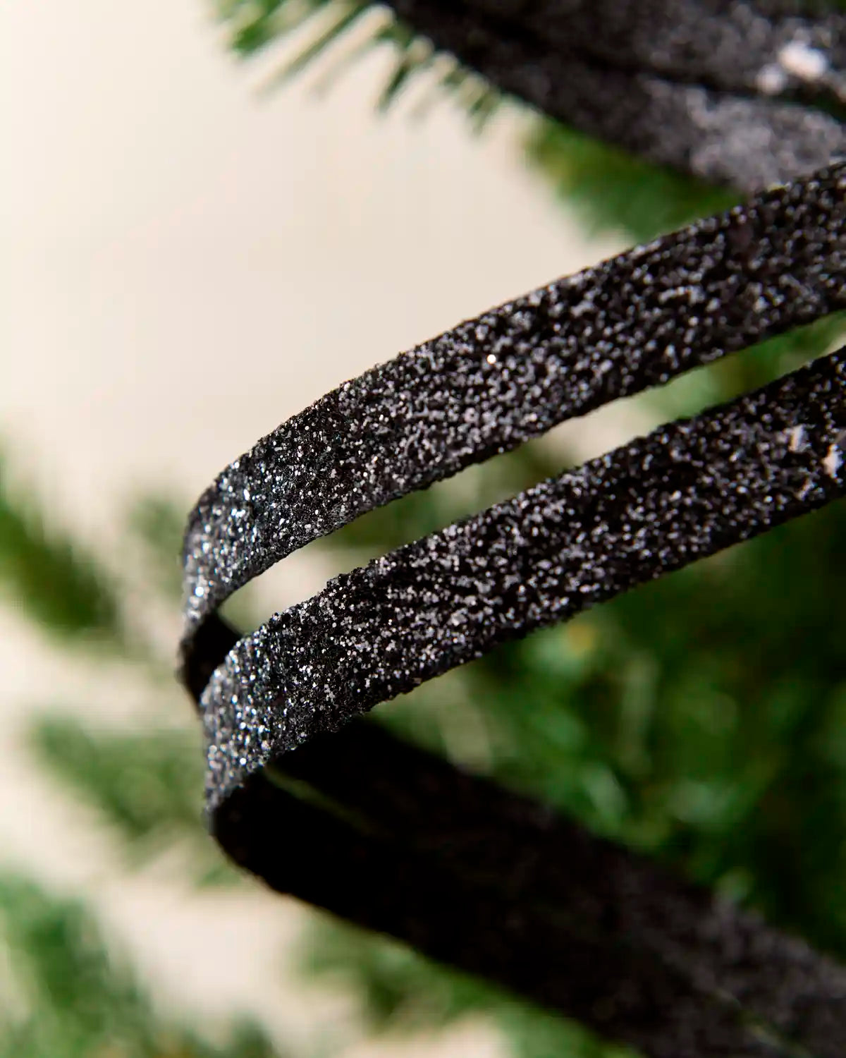 Close up black Glitter Spiral Swirl Pick showing black glitter details with green and cream blurred background