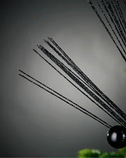Close-up of foliage portion of black glitter bauble spray in front of grey background