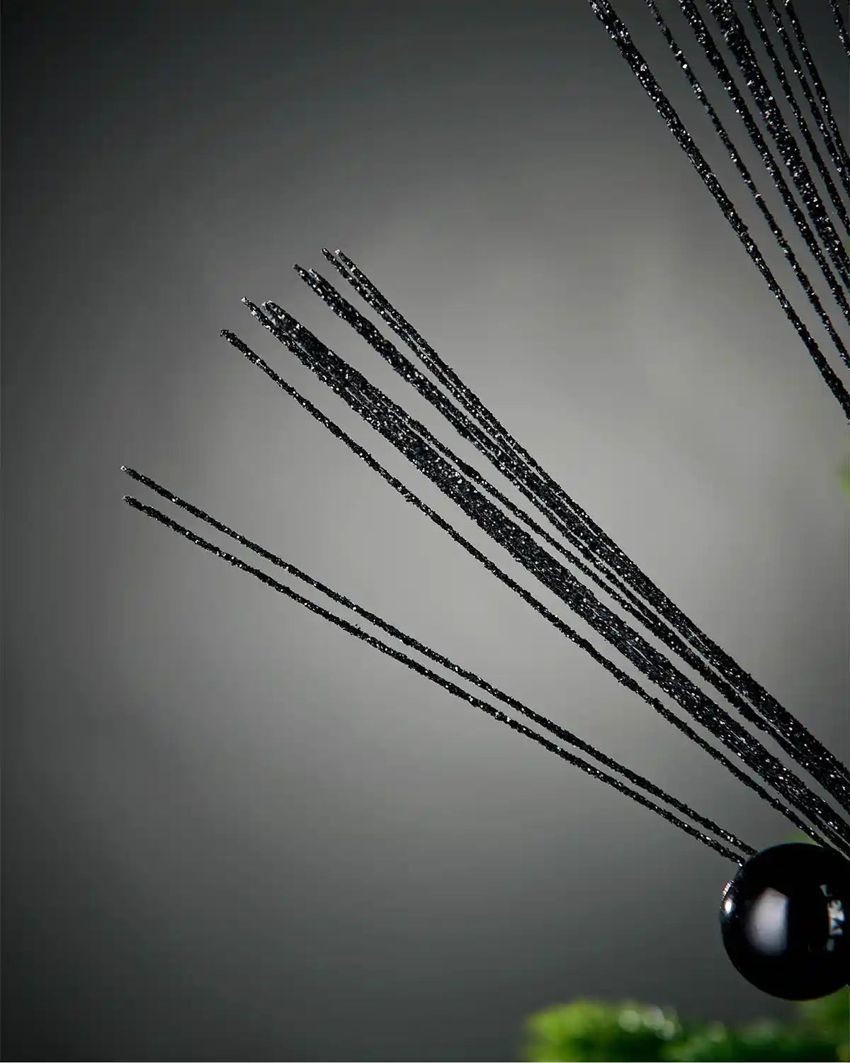 Close-up of foliage portion of black glitter bauble spray in front of grey background