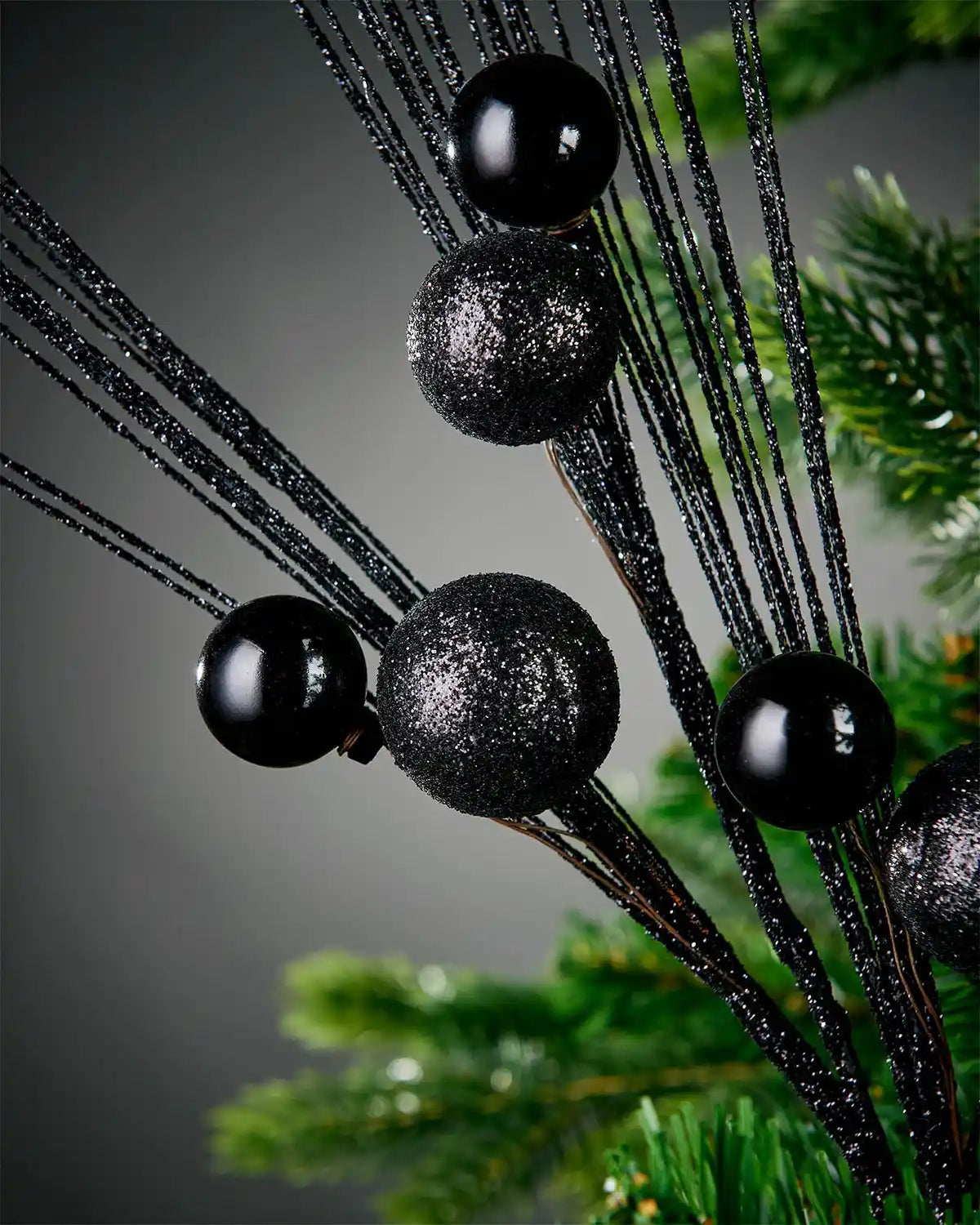 Close-up image of black glitter bauble spray attached to tree with grey background