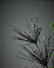 Close-up of black glitter firework spray in front of grey background highlighting sequin detail