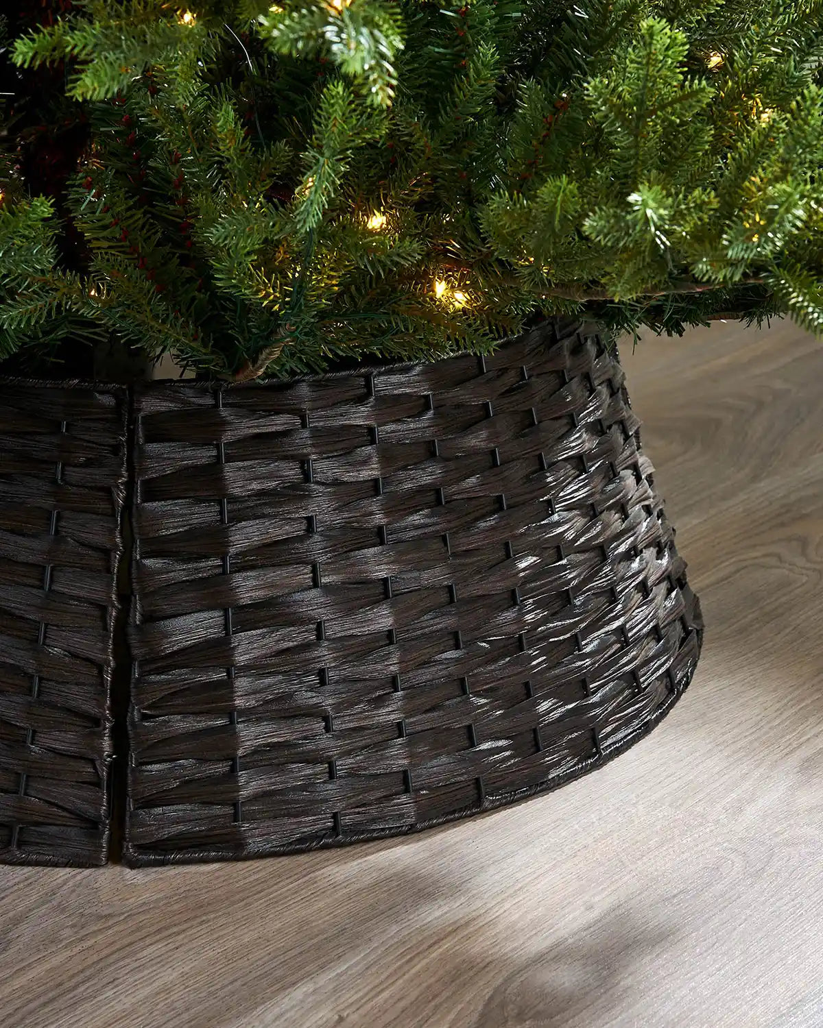 Close up dark brown woven tree collar around a decorated Christmas tree on a wooden floor.
