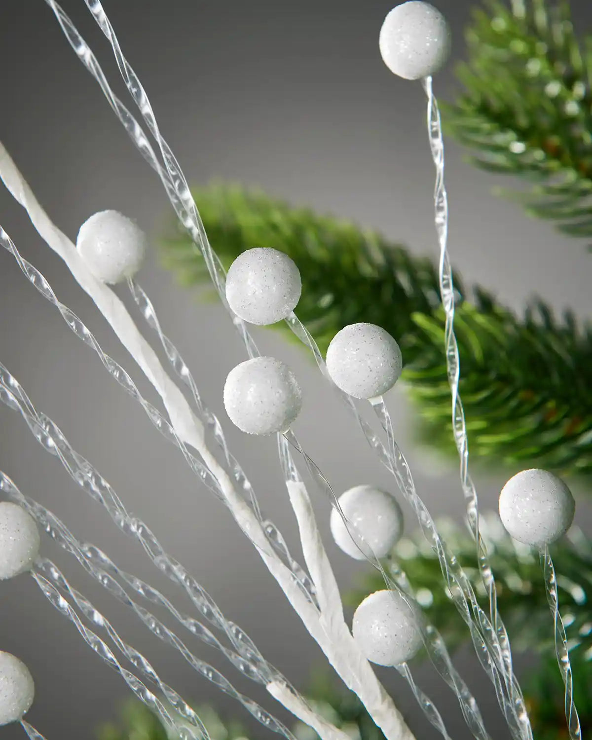 Close up decorative branch with white spherical berries against a blurred Christmas tree background