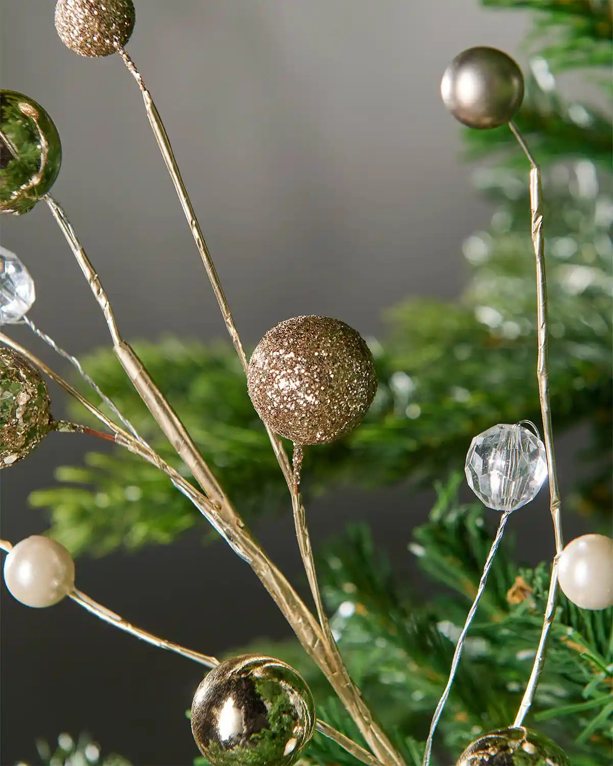 Close-up of gold bauble and jewelled spray on Christmas tree in front of grey wall background