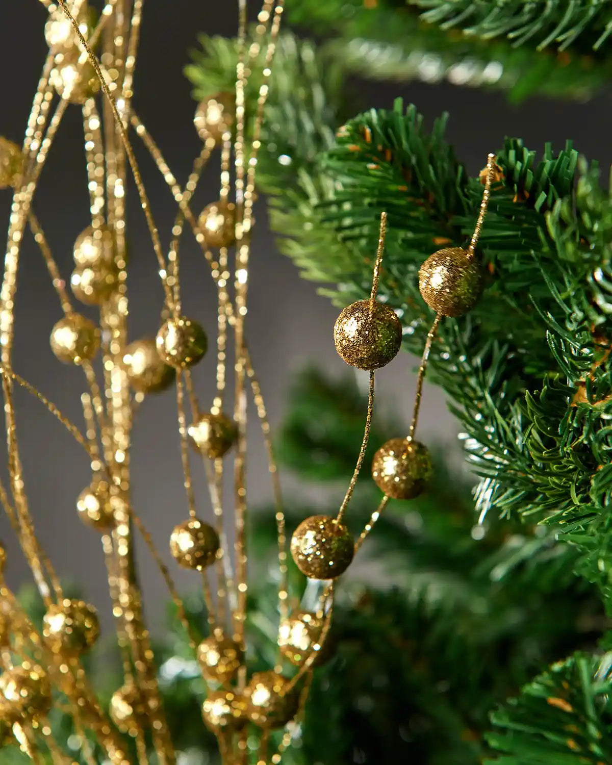 Close-up of the gold glitter berry spray attached to Christmas tree in front of grey wall background