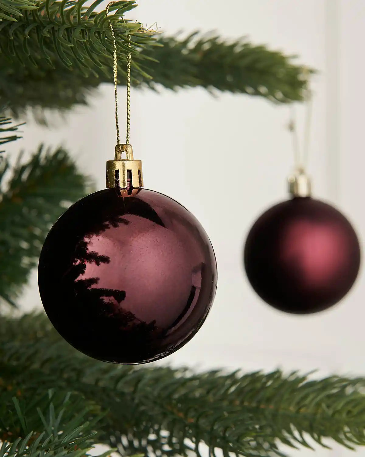 Close up of 3 burgundy baubles on a Christmas tree branch with blurry background