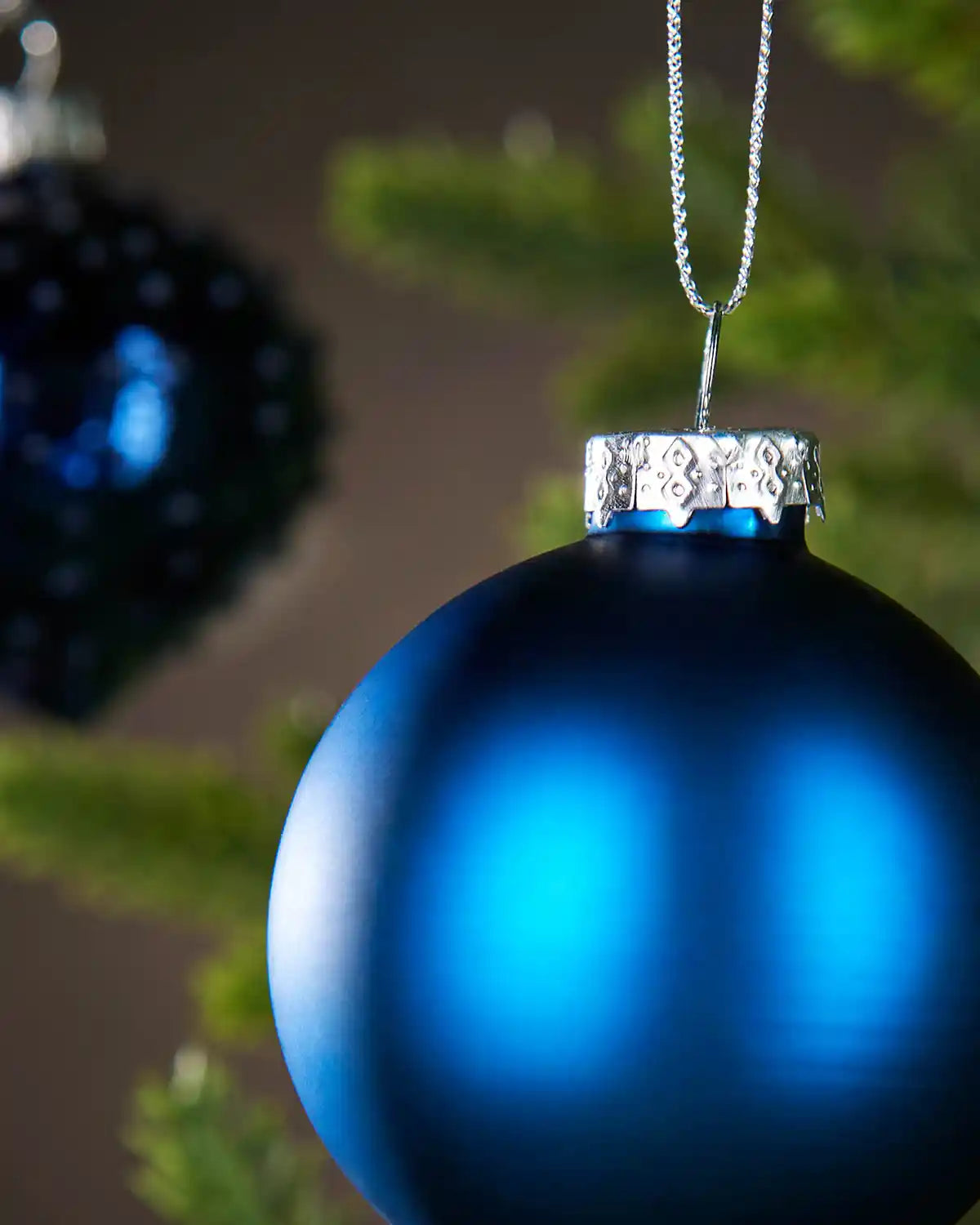 Close up of Blue Christmas baubles with silver cap on a blurred green background