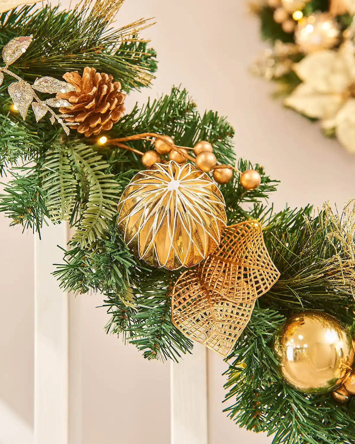 Close up of Christmas garland with gold baubles and pine cones on a cream wooden staircase banister