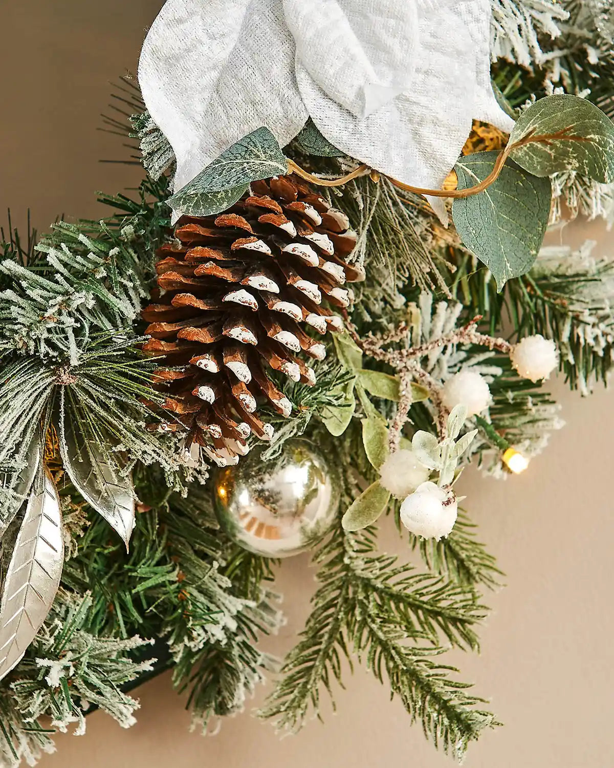 Close up of Christmas garland with pine cones, berries, and lights on a neutral background