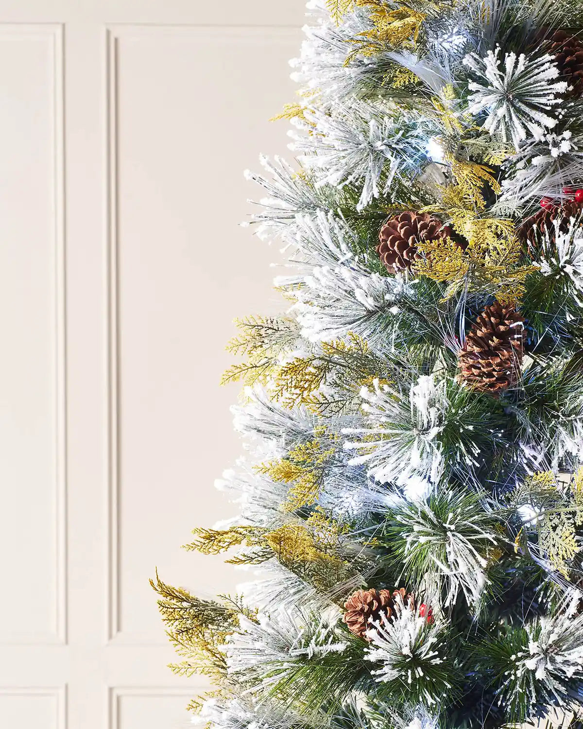 Close up of Decorated Christmas tree with Red berries, pinecones and white lights on a cream panel wall