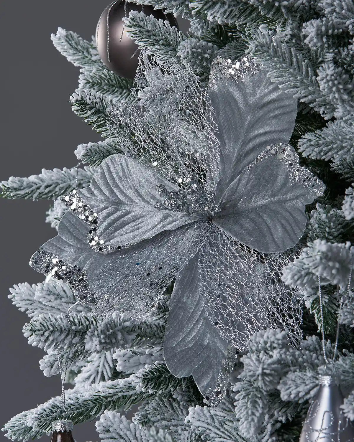 Close up of Decorative Poinsettia flower with silver lace-like petals on a white Christmas tree and silver baubles