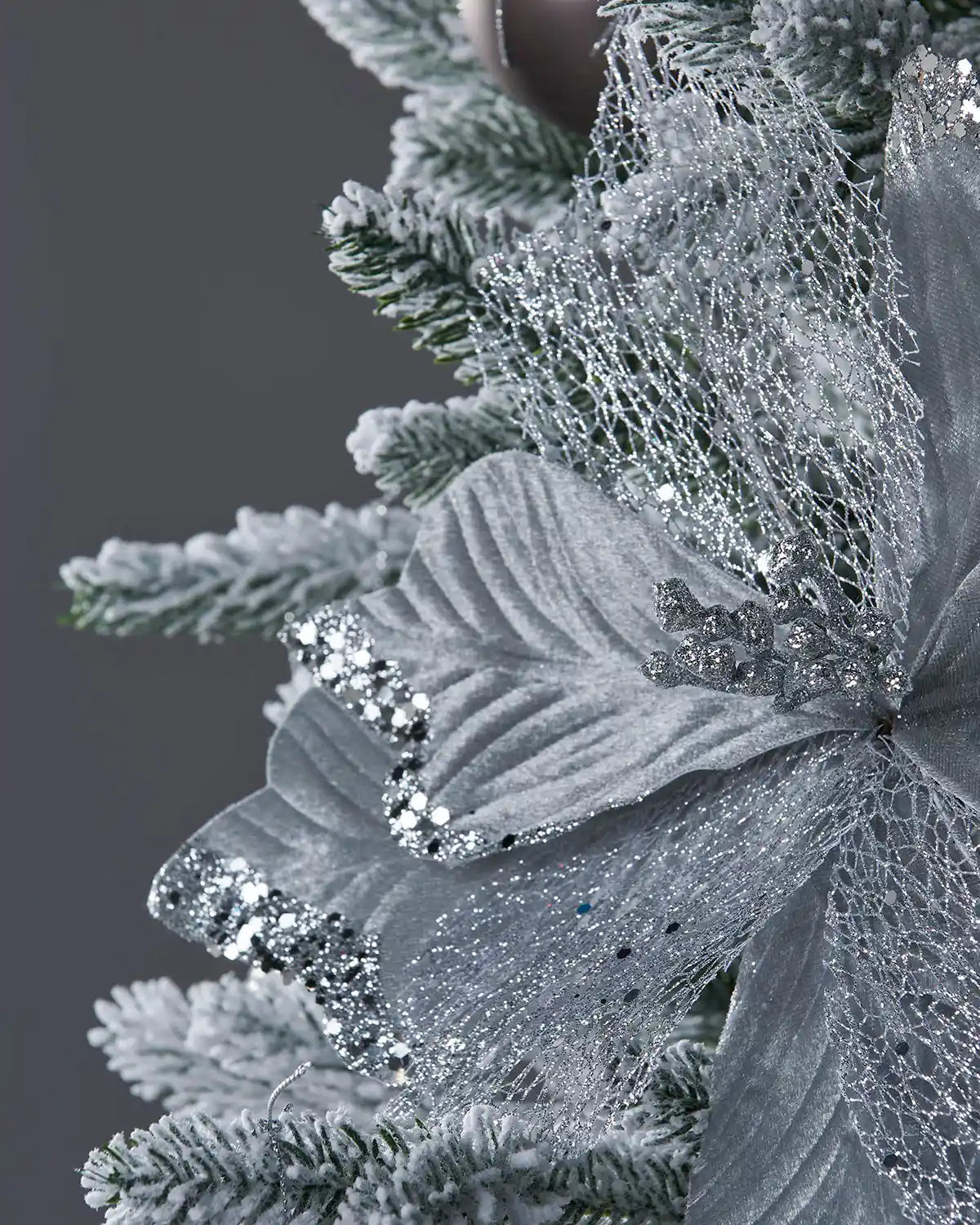 Close up of Decorative Silver Poinsettia flower with glitter berries inside flower on a white Christmas tree and silver baubles
